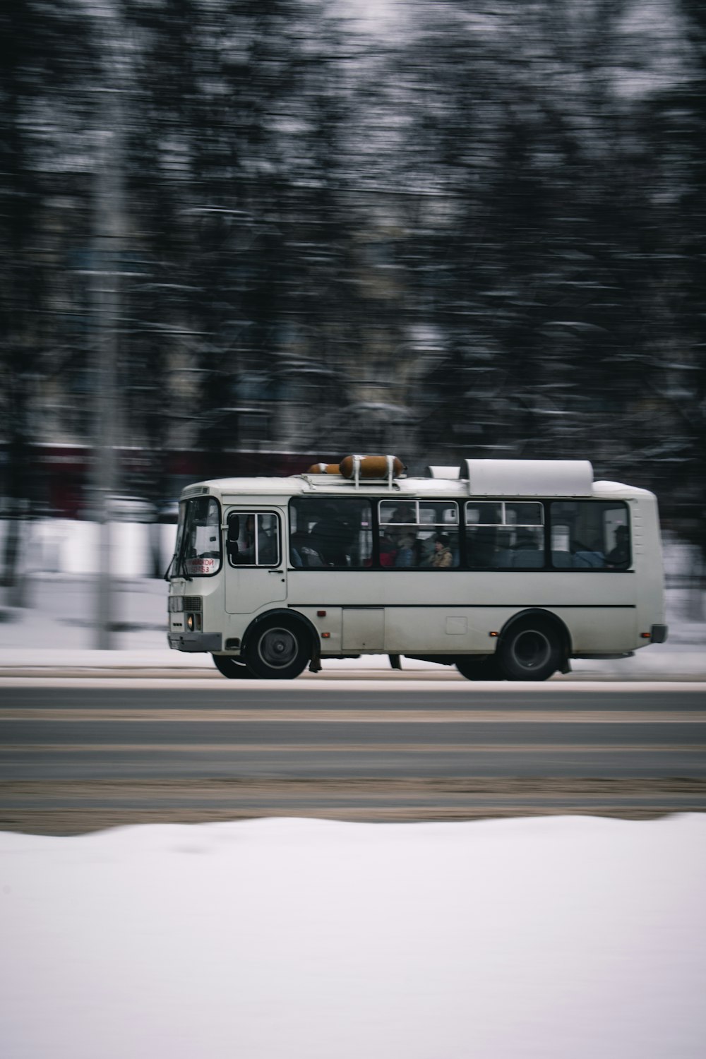 white bus passing trees beside road