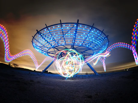 A glowing circular lens with electric blue light trails stretching toward a dark horizon under a metallic silver sky.