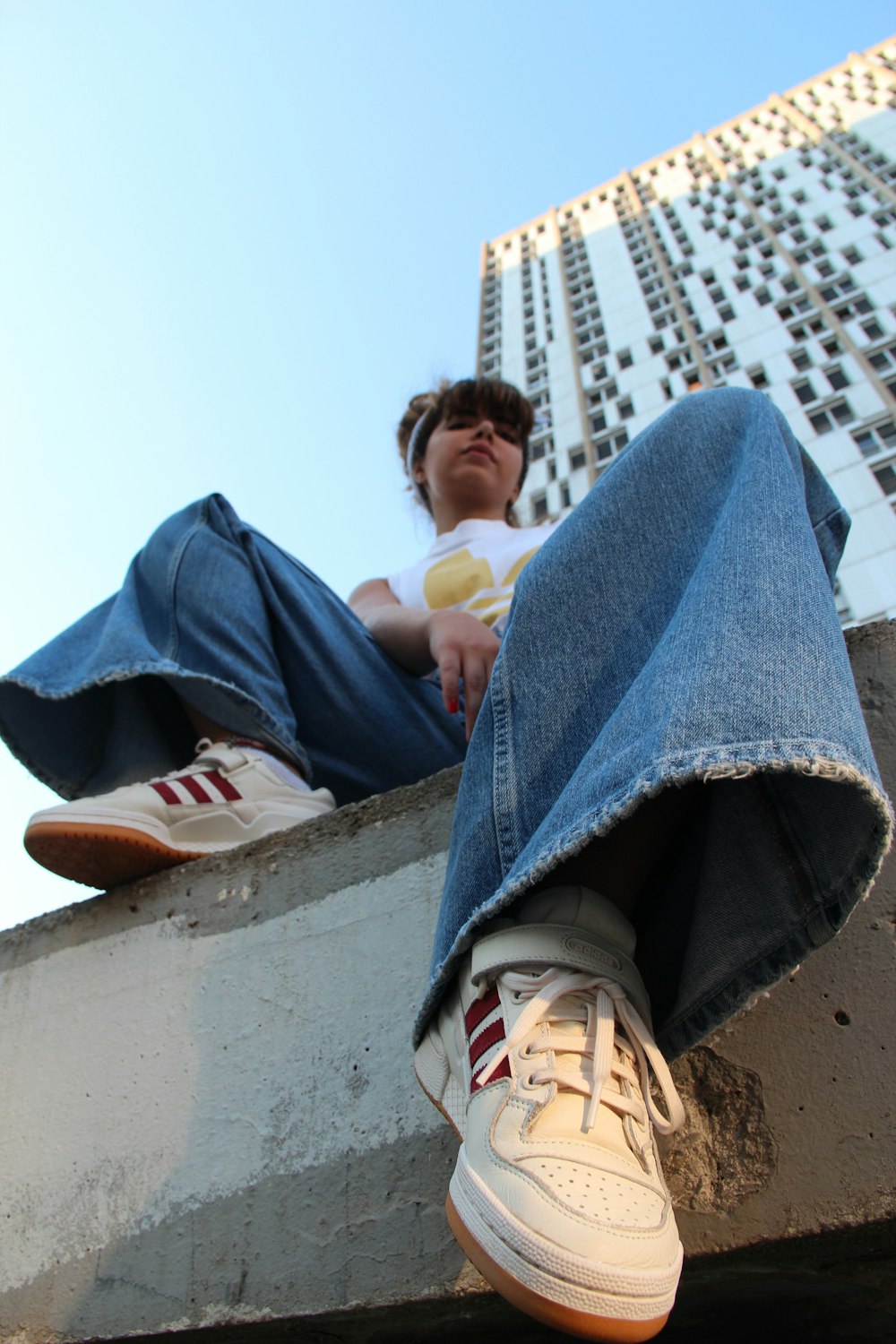 woman in white shirt and blue jeans sitting by edge of avement