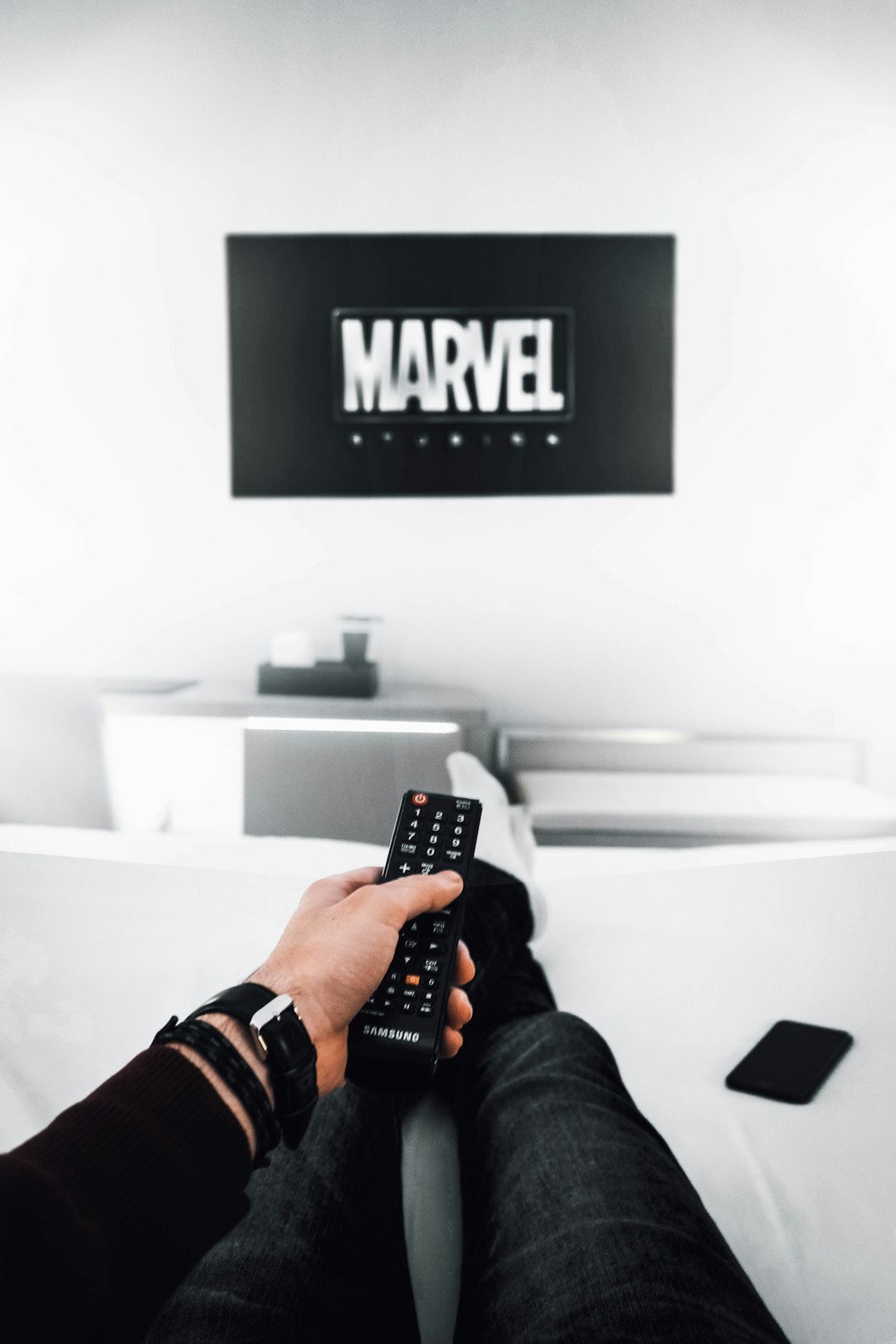 man holding remote control with Marvel logo on TV