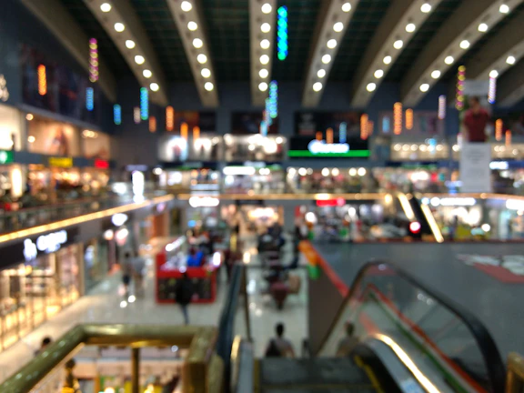 A wide, photorealistic view of a softly lit, modern mall interior with blurred bokeh effects.