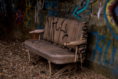 Close-up of a worn-out sofa before restoration, showing faded fabric and sagging cushions.