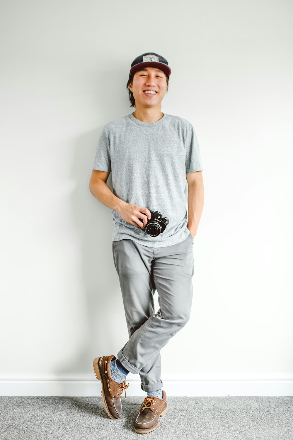 man standing and leaning by wall while holding camera