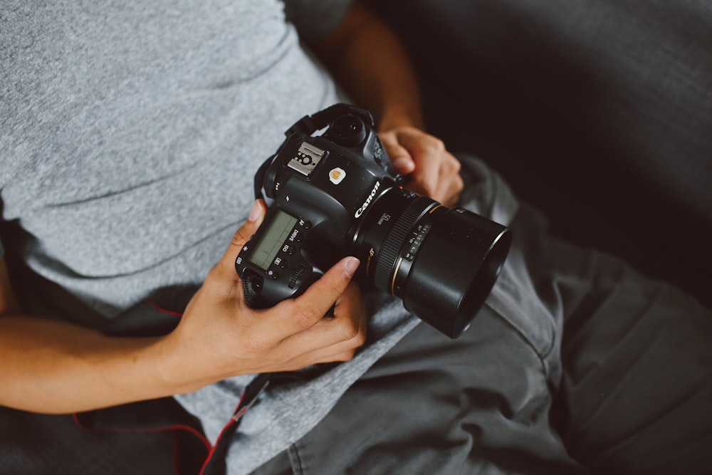 person in gray shirt holding black DSLR camera