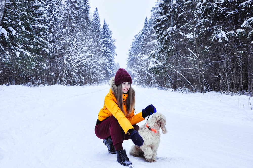 woman sitting beside dog surrounded by trees covered with snow