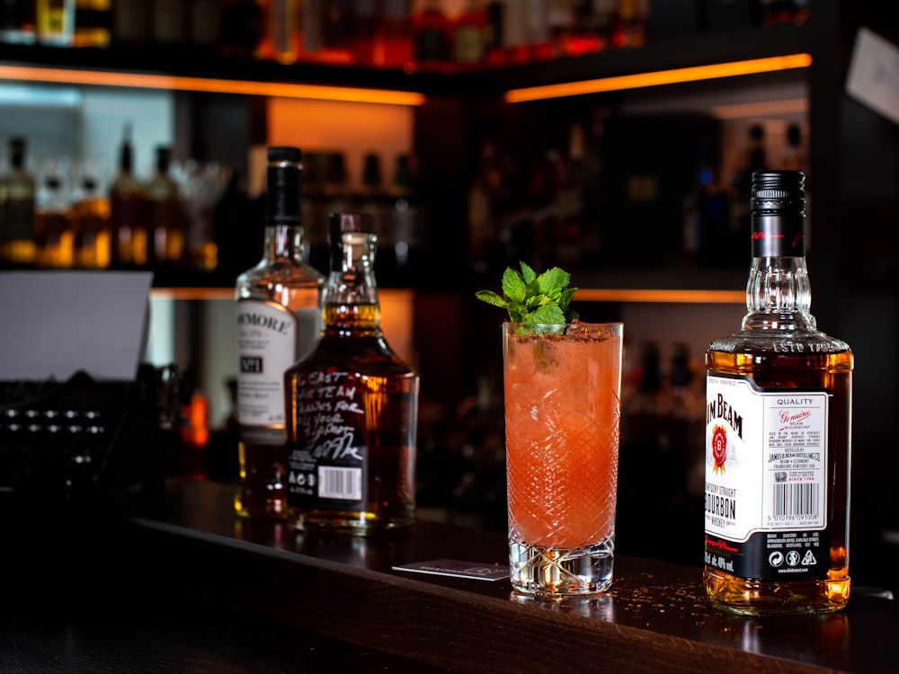 three liquor bottles and cocktail drink on bar counter