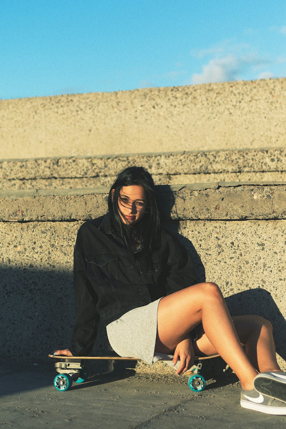 woman sitting on skateboard leaning on concrete wall