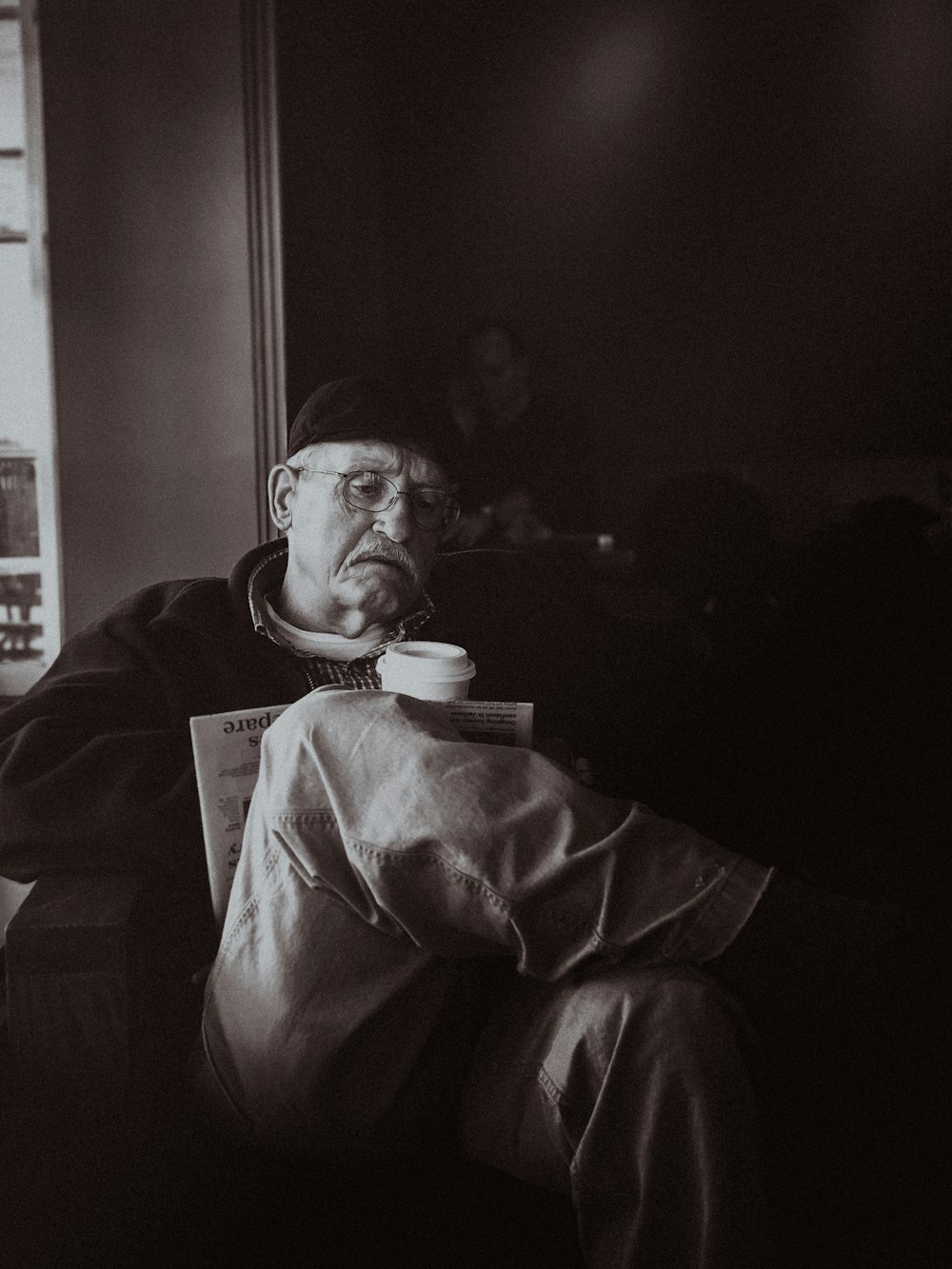 grayscale photography of man sitting on sofa chair holding coffee cup
