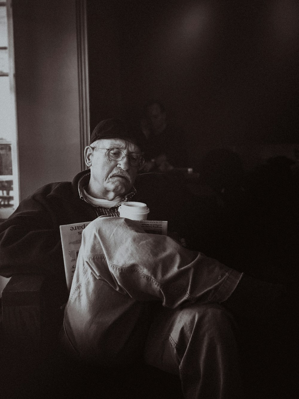 Photographie en niveaux de gris d’un homme assis sur une chaise de canapé tenant une tasse de café