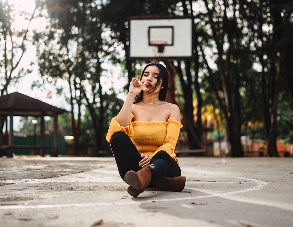 woman sitting while eating lollipop in basketball court