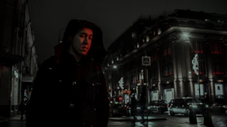 Volunteers in black hoodies handing out meals to people on a dimly lit urban street at night.