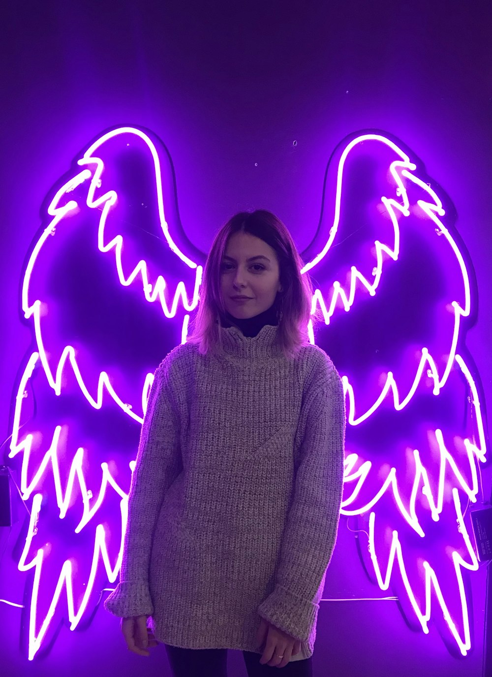 woman standing in front of purple wings neon light