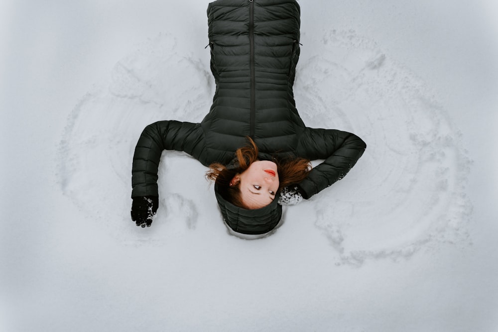 woman wearing black jacket lying on snow