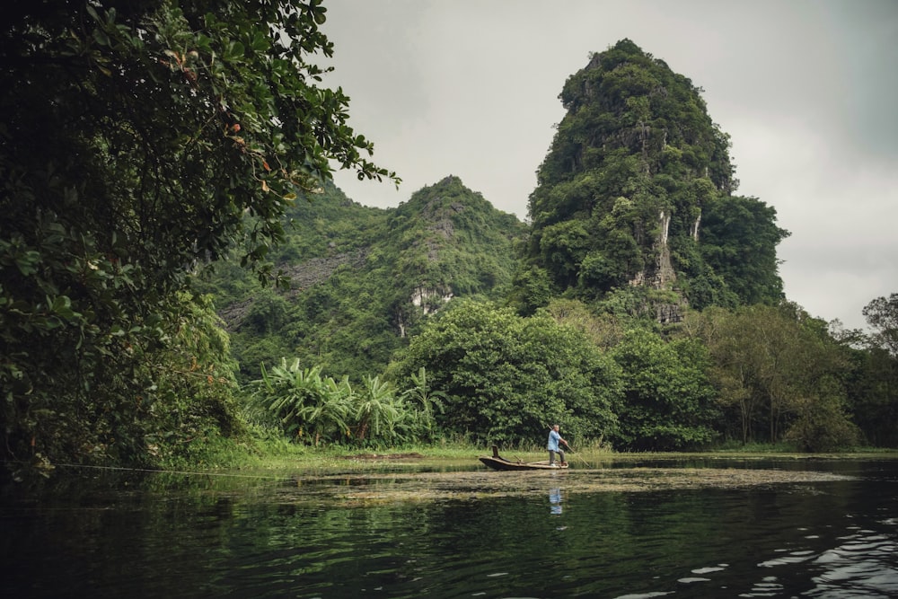 person riding boat on body of water beside trees