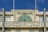 An old building featuring a decorative facade with a peacock design. The structure has large windows and visible weathering on the concrete. Above the windows, there is a sign with the words 'Novidade! Armazens Cunhas'. The building's design reflects vintage architectural styling.
