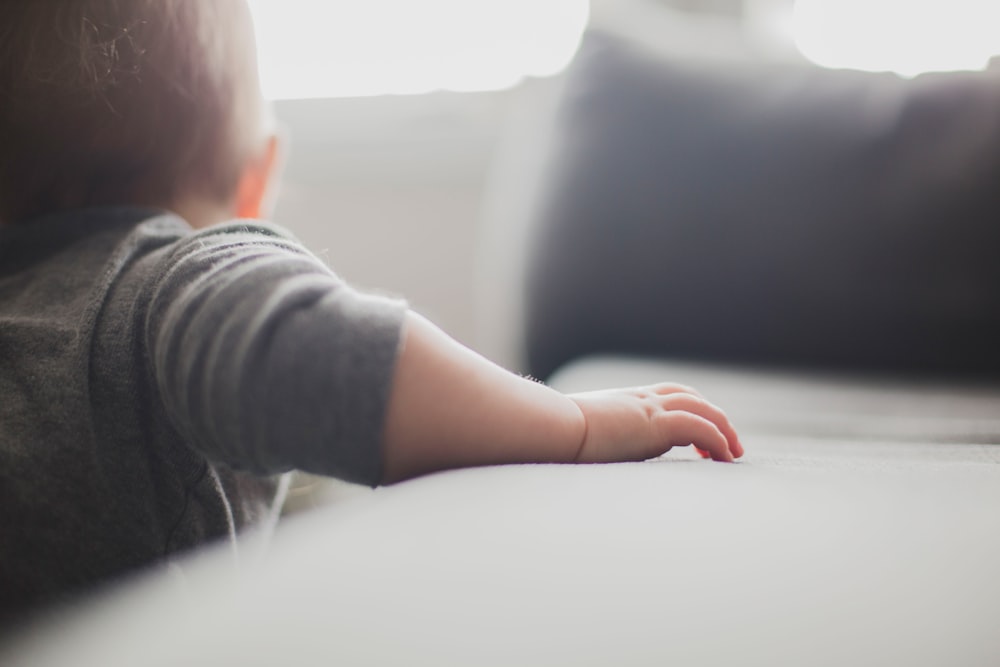 toddler wearing gray shirt holding on to sofa