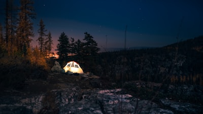 A camping scene at twilight illuminated by the warm beam of a camping pockets flashlight.