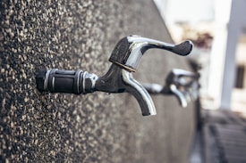 A close-up view of a row of metallic faucets protruding from a textured wall, showing a focus on industrial design with an emphasis on the reflective surface of the taps.