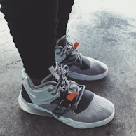 A pair of sleek black running shoes with orange accents on a concrete path surrounded by greenery.