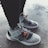 A pair of stylish, modern sneakers featuring gray and black accents with orange tags. The shoes have a sleek design, showcased on a textured concrete floor.