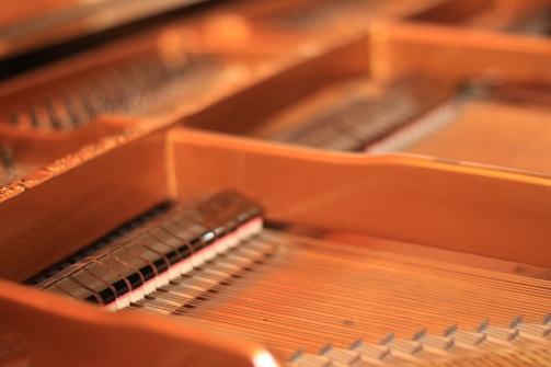 A close-up view of the inside of a piano, showcasing the strings and hammers. The warm wood tones and metallic strings are prominently featured, highlighting the intricate craftsmanship of the instrument.