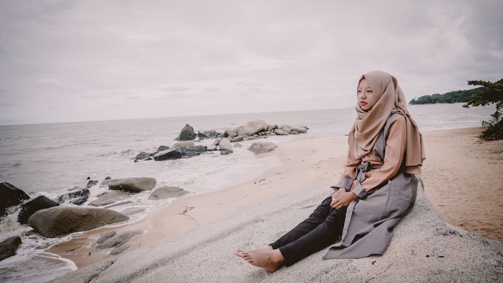 woman wearing hijab scarf and black pants sitting on shore