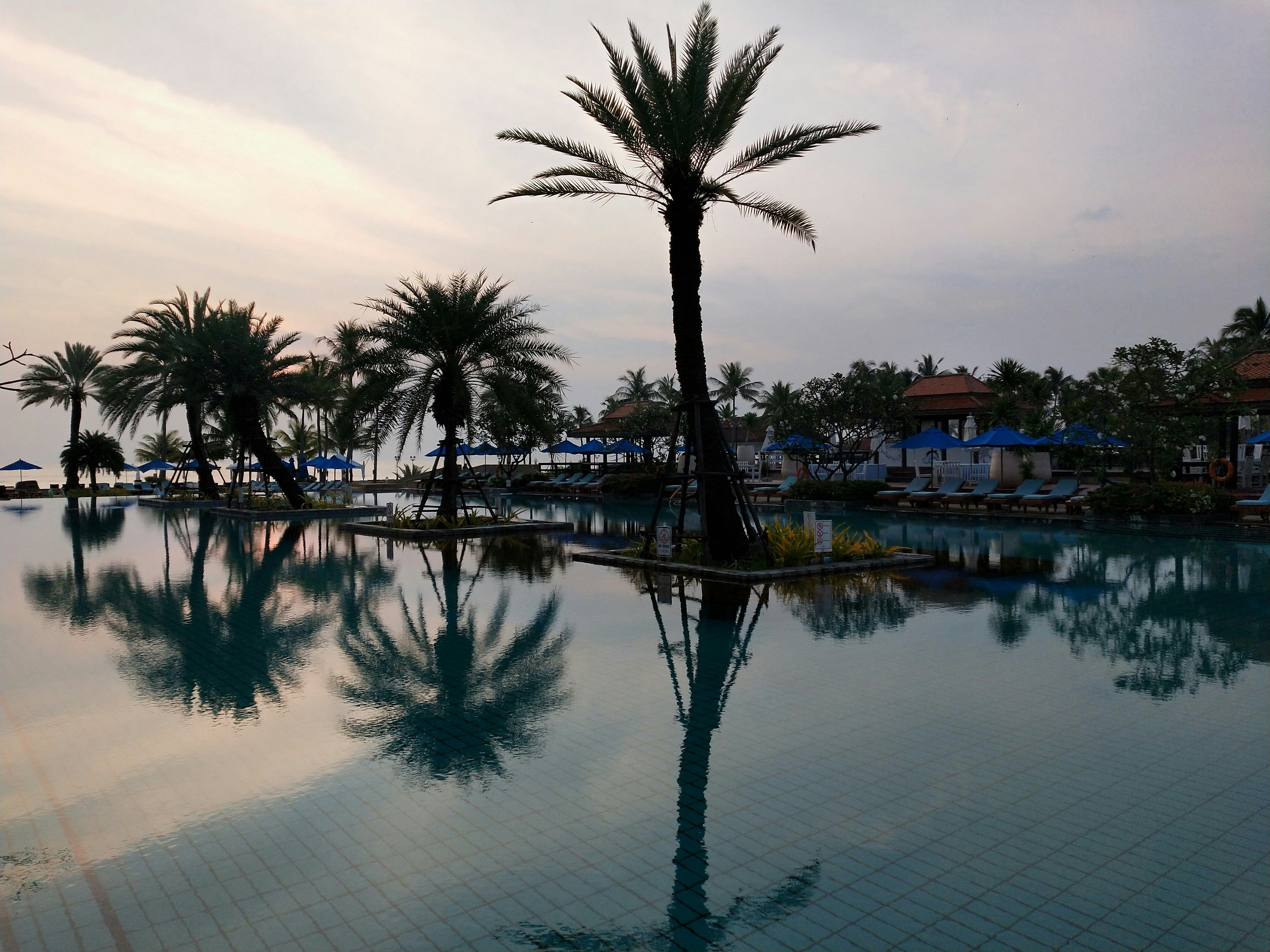 Outdoor swimming pool with clear blue water, dim poolside lighting, dark evening atmosphere, moody reflections