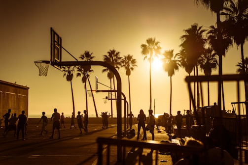 A basketball team practicing drills on an outdoor court during sunset.