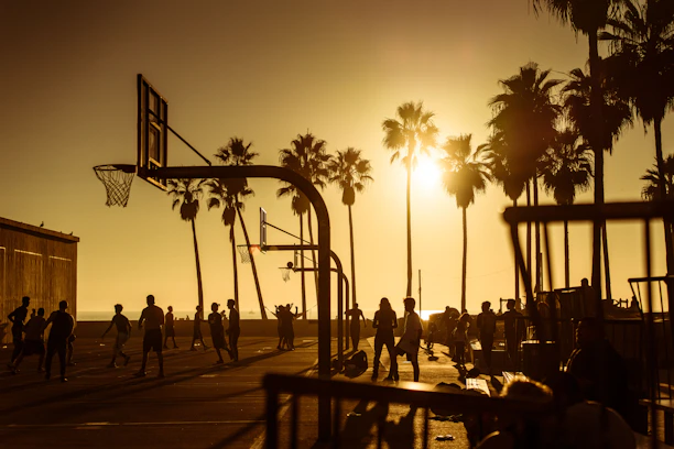 A group of young players and coaches sharing a high-five on an outdoor basketball court at sunset.