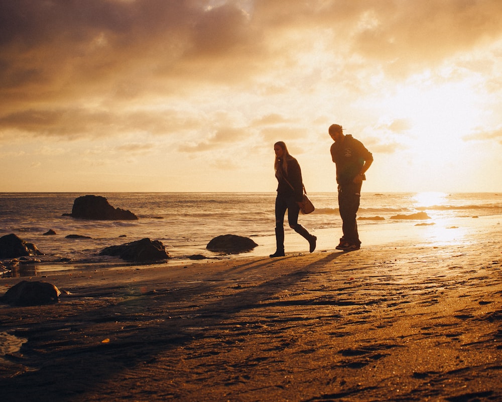 man and woman walking on seashore during sunset