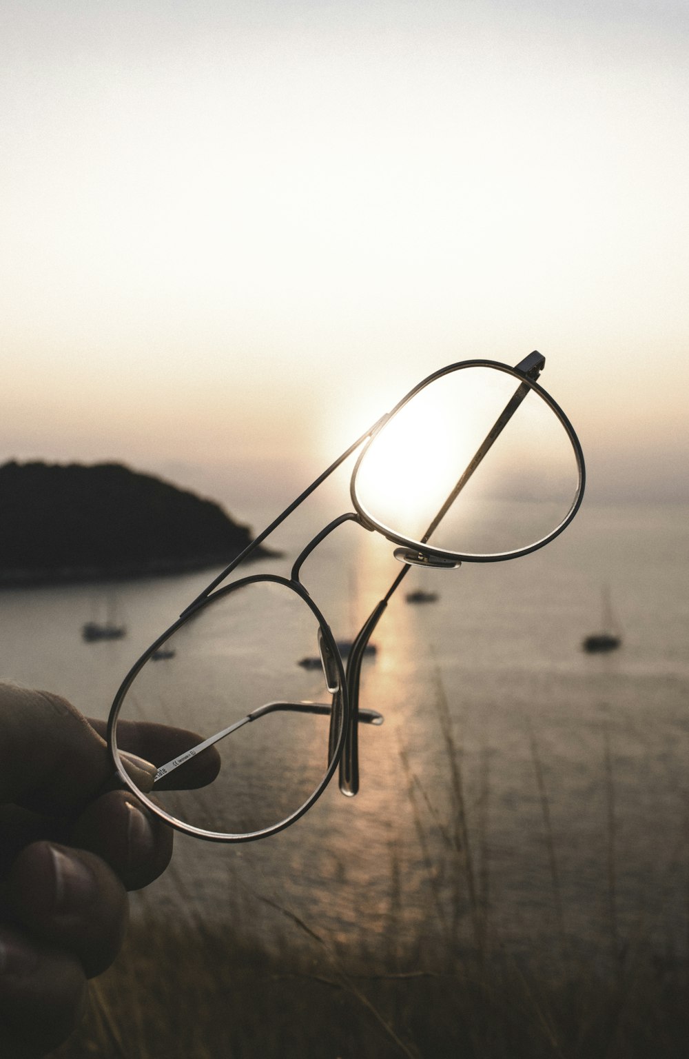 person holding gray framed eyeglasses near body of water