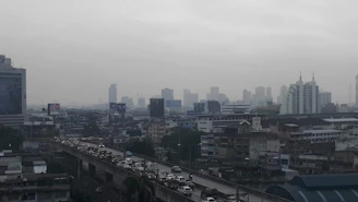 A congested city street filled with cars emitting visible exhaust fumes under a gray sky.