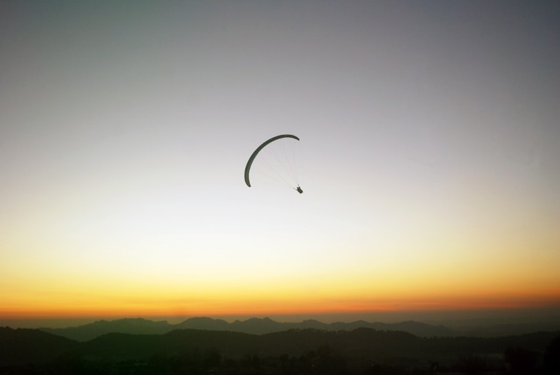 Paraglider soaring over the Cerro Arco with Mendoza city below at sunset.