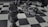 Close-up of a dark wooden chess king piece standing prominently in the foreground on a checkerboard pattern surface, with several other chess pieces blurred in the background lying on their sides.