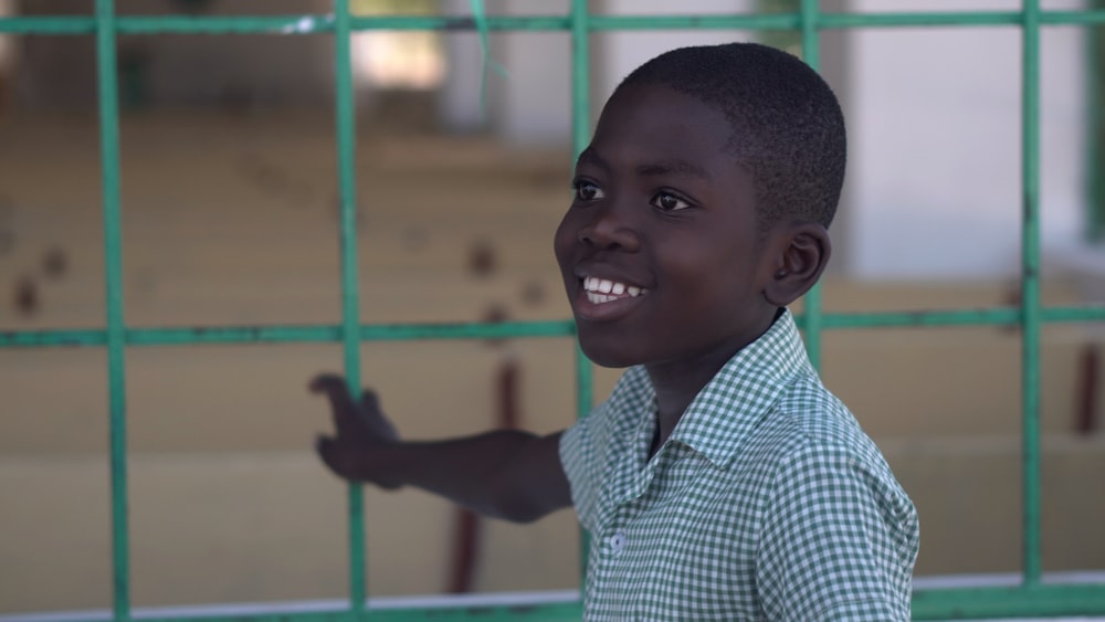 smiling boy standing and holding green metal fence