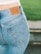A close-up view of a person wearing a pair of blue Levi Strauss & Co. jeans, showcasing the iconic brown leather label on the waistband and a red tag on the pocket. The background features a blurred green area, possibly grass.