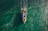 A small fishing boat navigates through vibrant, teal waters, creating ripples as it moves. The boat is filled with fishing gear and a few people, with its bright colors contrasting against the sea.