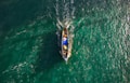 A small fishing boat navigates through vibrant, teal waters, creating ripples as it moves. The boat is filled with fishing gear and a few people, with its bright colors contrasting against the sea.