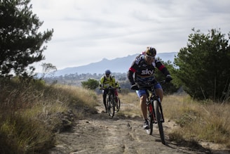 Cyclists riding along a rugged mountain trail under a clear blue sky.