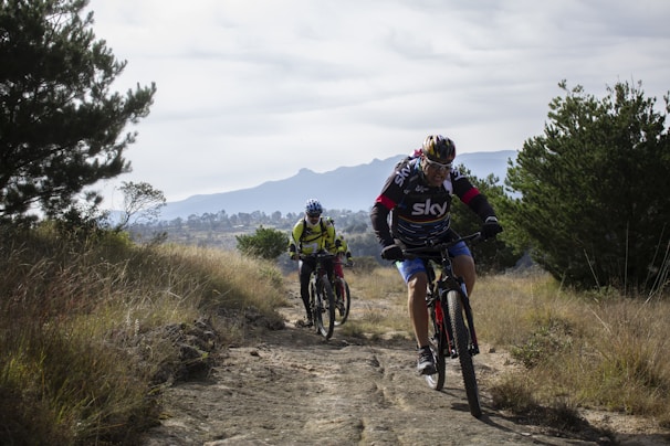 Cyclists riding along a rugged mountain trail under a clear blue sky.