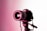 A professional camera mounted on a tripod is highlighted under pink lighting. The focus is on the lens, which has visible brand markings and intricate details that are illuminated against a white background.
