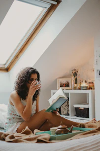 woman holding a book and drinking from a mug
