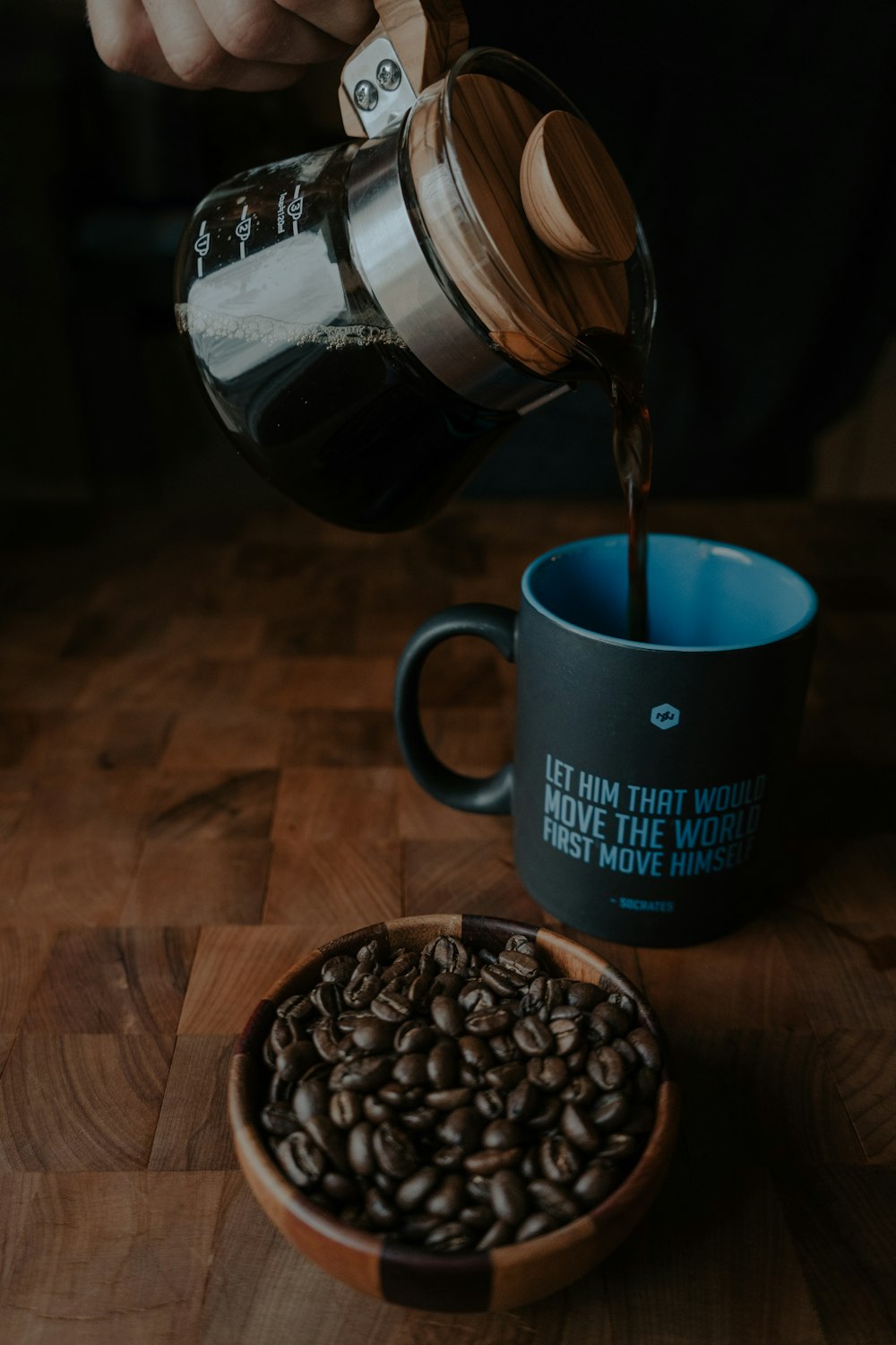 Persona que vierte café en una taza negra al lado de los granos de café