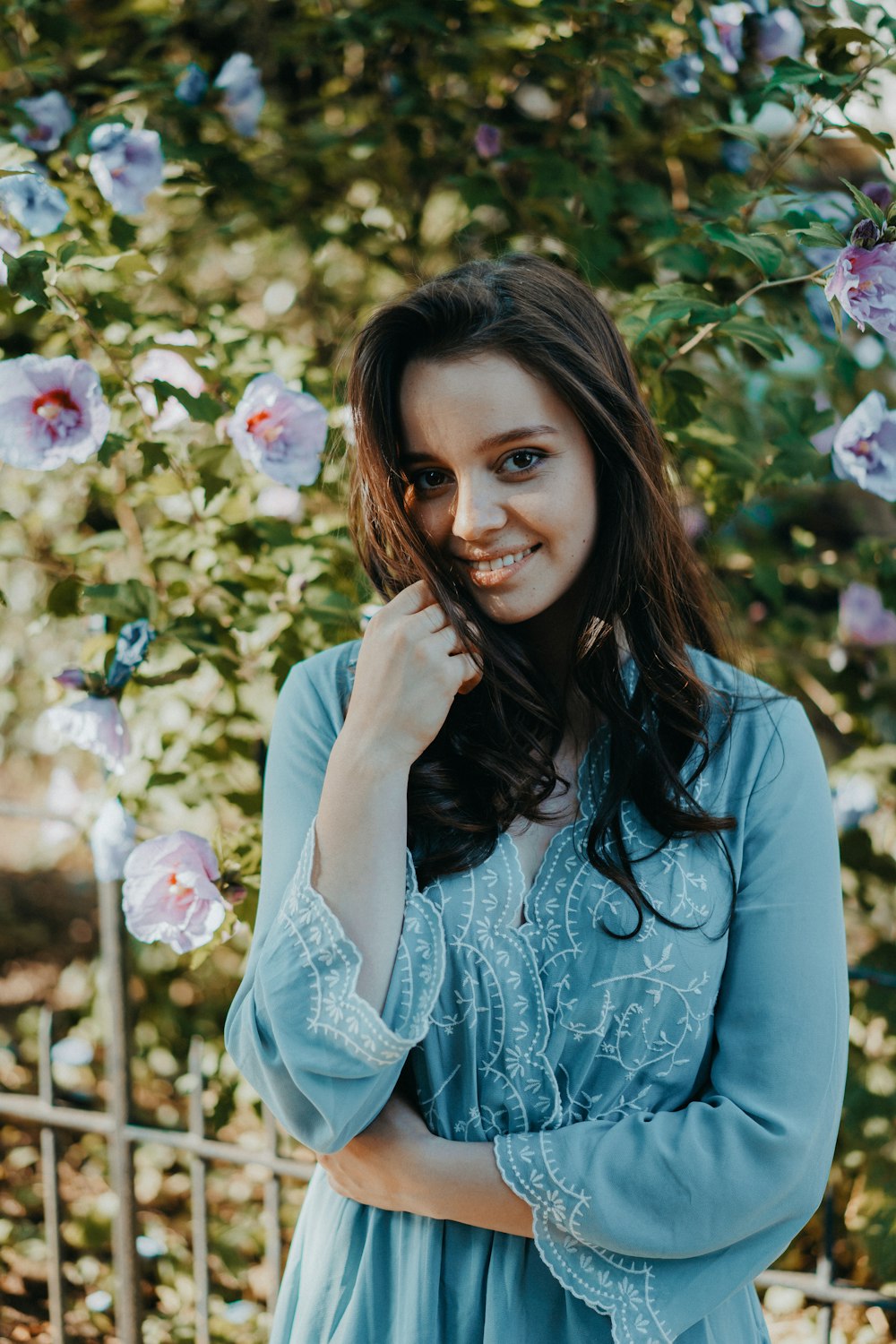 woman wearing blue long-sleeved top standing beside white flowers