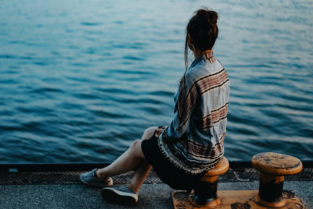 woman sitting on yellow metal post front of sea