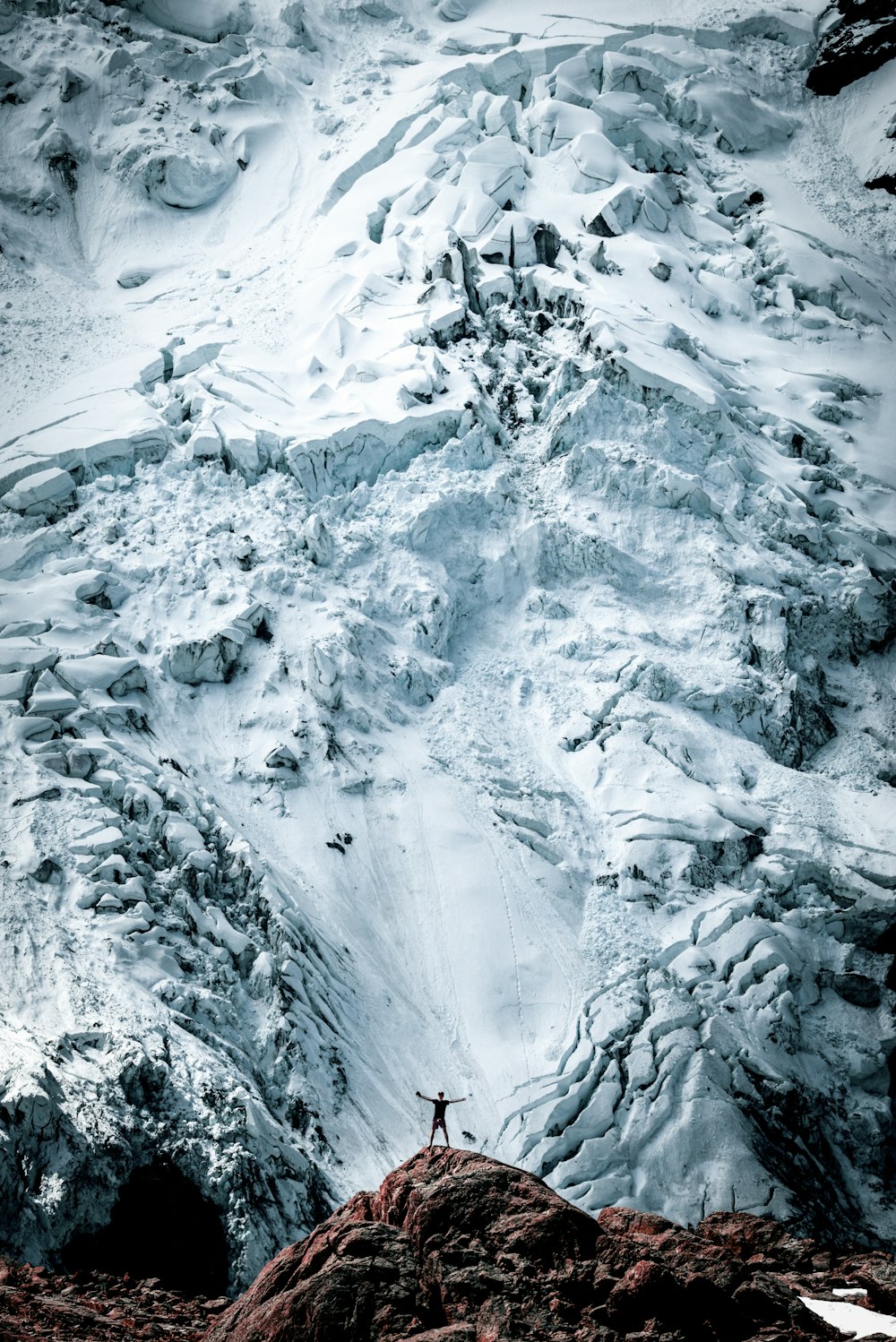 自然写真の雪をかぶった山の岩の正面に立つ人