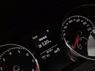 A close-up of a car dashboard displaying various gauges, including a speedometer and tachometer. The digital display reads a range of 520 km and shows time, temperature, and trip distance information. The gauges have white numbers and red needles on black backgrounds.