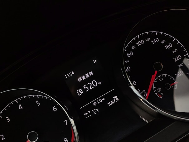 A close-up of a car dashboard displaying various gauges, including a speedometer and tachometer. The digital display reads a range of 520 km and shows time, temperature, and trip distance information. The gauges have white numbers and red needles on black backgrounds.