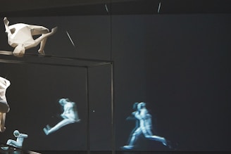 A surreal scene featuring a geometric, angular sculpture of a human figure positioned upside-down near the top left. In the background, a series of semi-transparent, dynamic images depict a human figure in various stages of running, conveying motion. The setting is mostly dark, emphasizing the light shapes and movement.