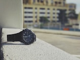 An urbantick watch resting on a concrete ledge with skyscrapers blurred behind.